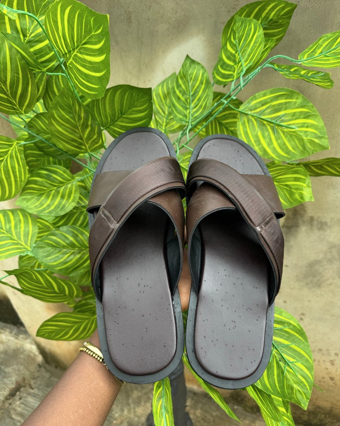 A pair of brown IRIS Africa textured cross slides held up against green leaves